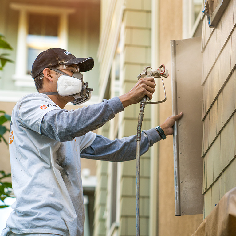 Mobile view of a pro painter spray painting the exterior wall of a house.
