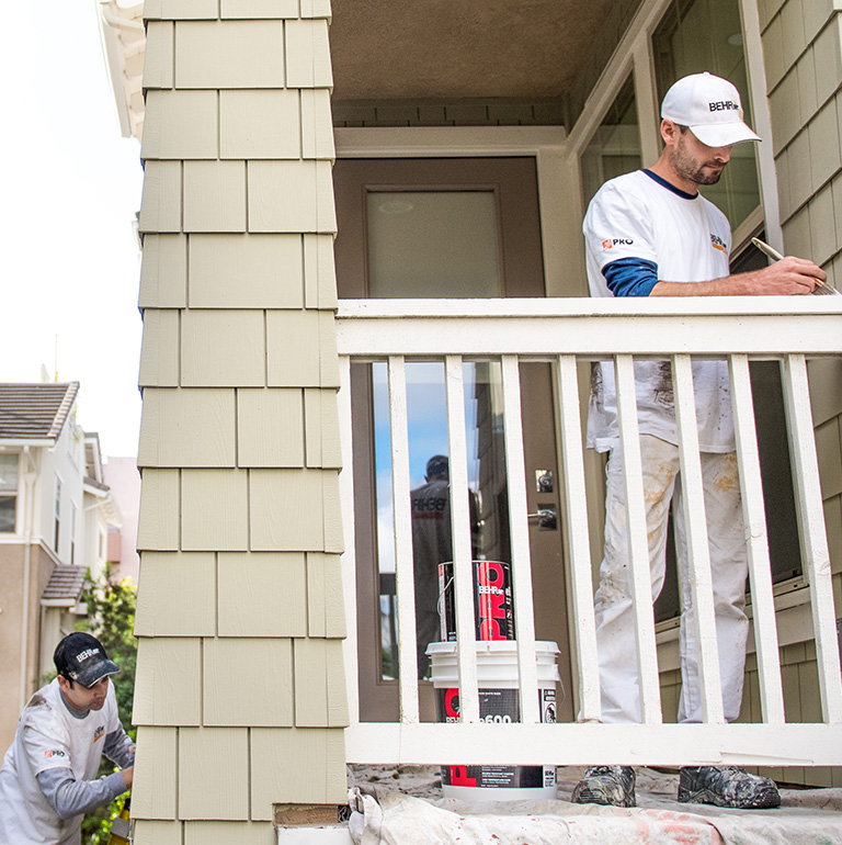 Small image of 2 Pro painters painting the wooden railings of the exterior of an apartment block