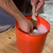 Cleaning paint brush in pail of soapy water.