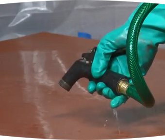 A person's hand wearing a rubber glove spraying water out of hose onto the ground