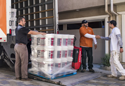 An image of a palette of BEHR PRO paint being delivered at a job site.  A Pro Painter is shaking the hand of a BEHR PRO Rep