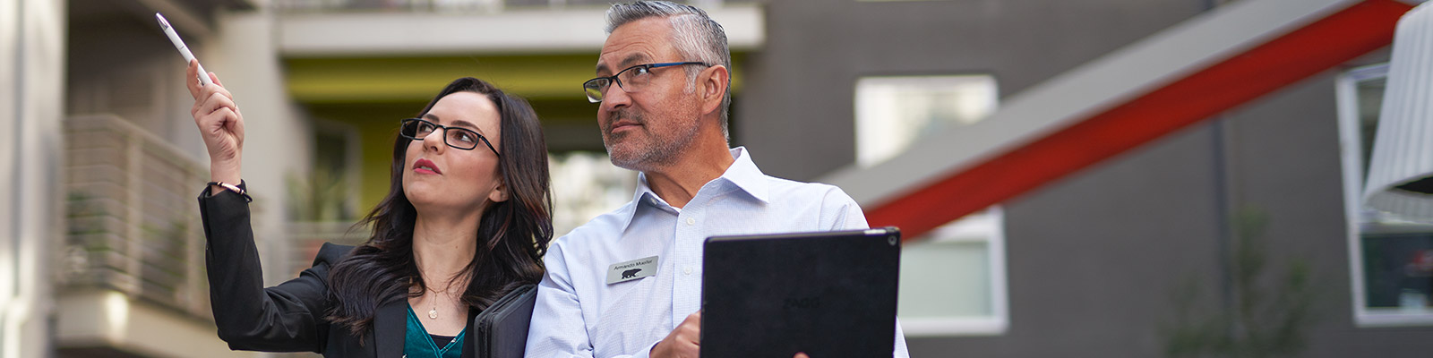 A close up image a property manager and a BEHR PRO Rep looking at what the property manager is pointing at on the outside of an apartment complex. The BEHR PRO rep is taking notes on an IPAD
