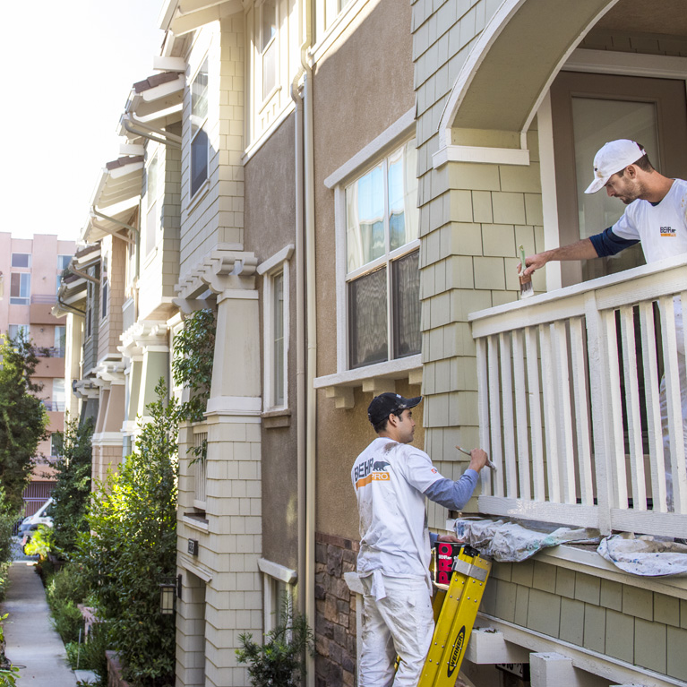 Small image of 2 Pro painters painting the wooden railings of the exterior of an apartment block