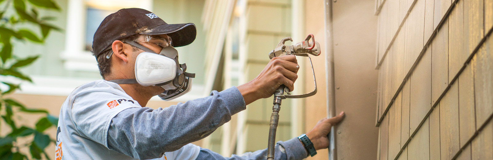 Desktop view of a pro painter spray painting the exterior wall of a house.