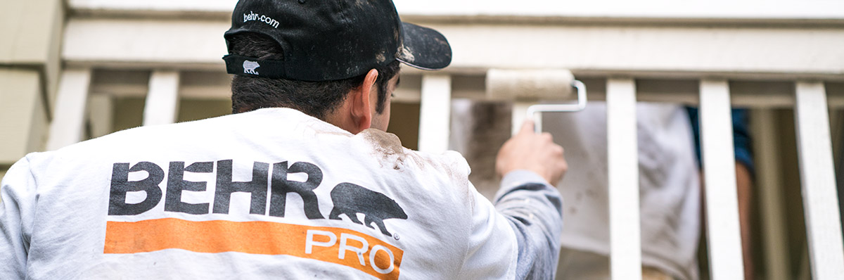 Large close up image of a back of a painting contractor who is painting with a roller with the logo of BEHR PRO imprinted on the shirt.