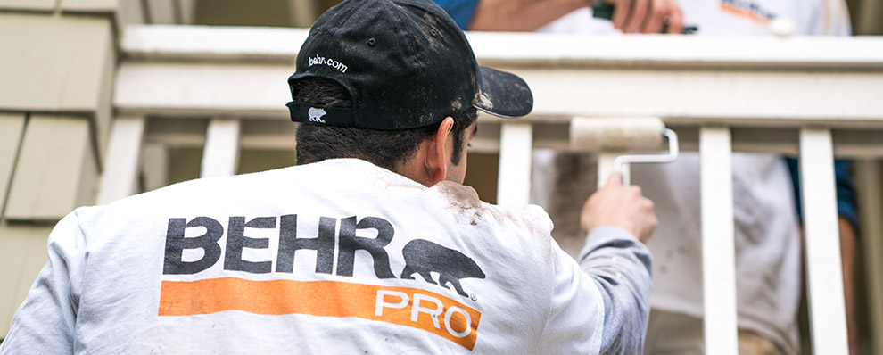 Small A close up image of a back of a painting contractor who is painting with a roller with the logo of BEHR PRO imprinted on the shirt.