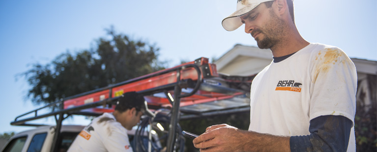 Painting contractor with a BEHR PRO shirt checking his mobile phone