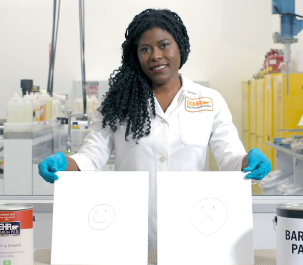 A Behr employee in a lab coat holding 2 boards