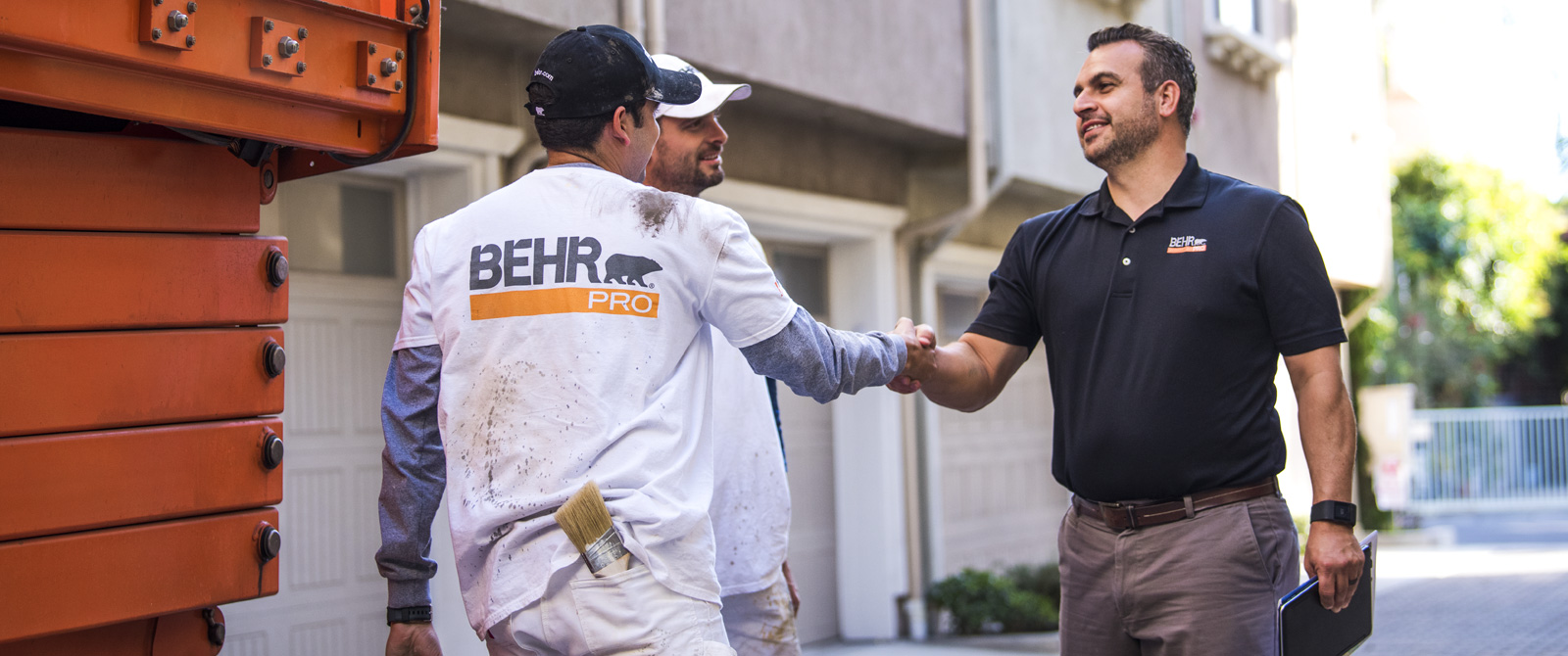 A BEHR PRO Rep shaking hands with on of the 2 Pro Painters. In the background is a multi family condo units.