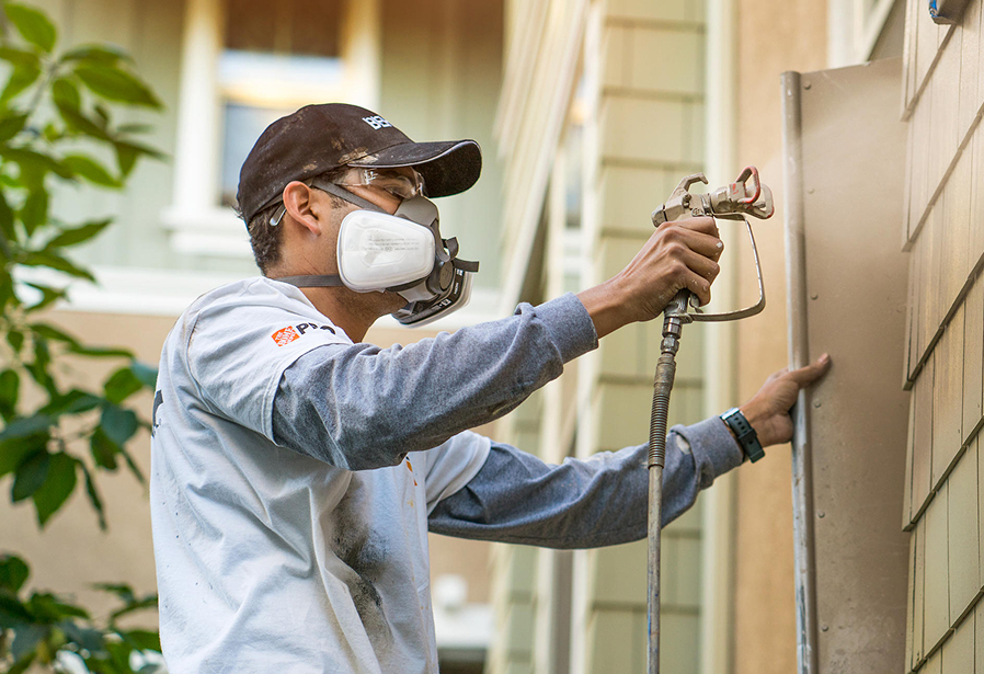 Pro Contractor spray painting the exterior wall of a house.