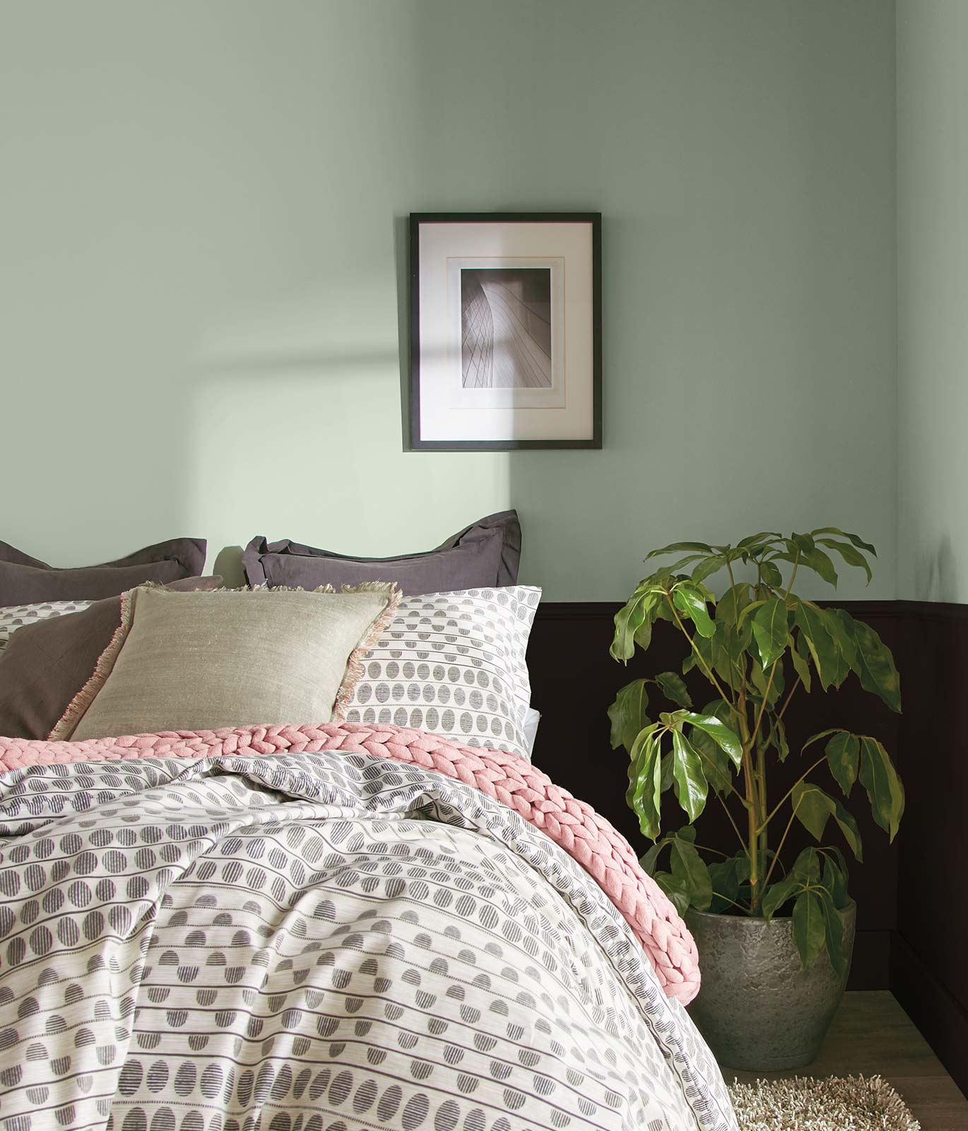 Tight crop of a bedroom with gray and white bedding. Upper half of the walls are painted in a light green. The bottom half is painted black. The feel of the room is calming.