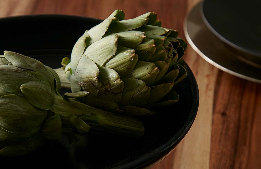 A bowl filled with untouched artichokes waiting to be cooked, the atmosphere is quiet and calm.