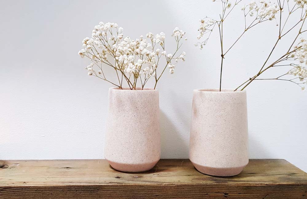 Two vases with white small flowers sitting on a wood shelf. Flowers in vase are soft and subtle.