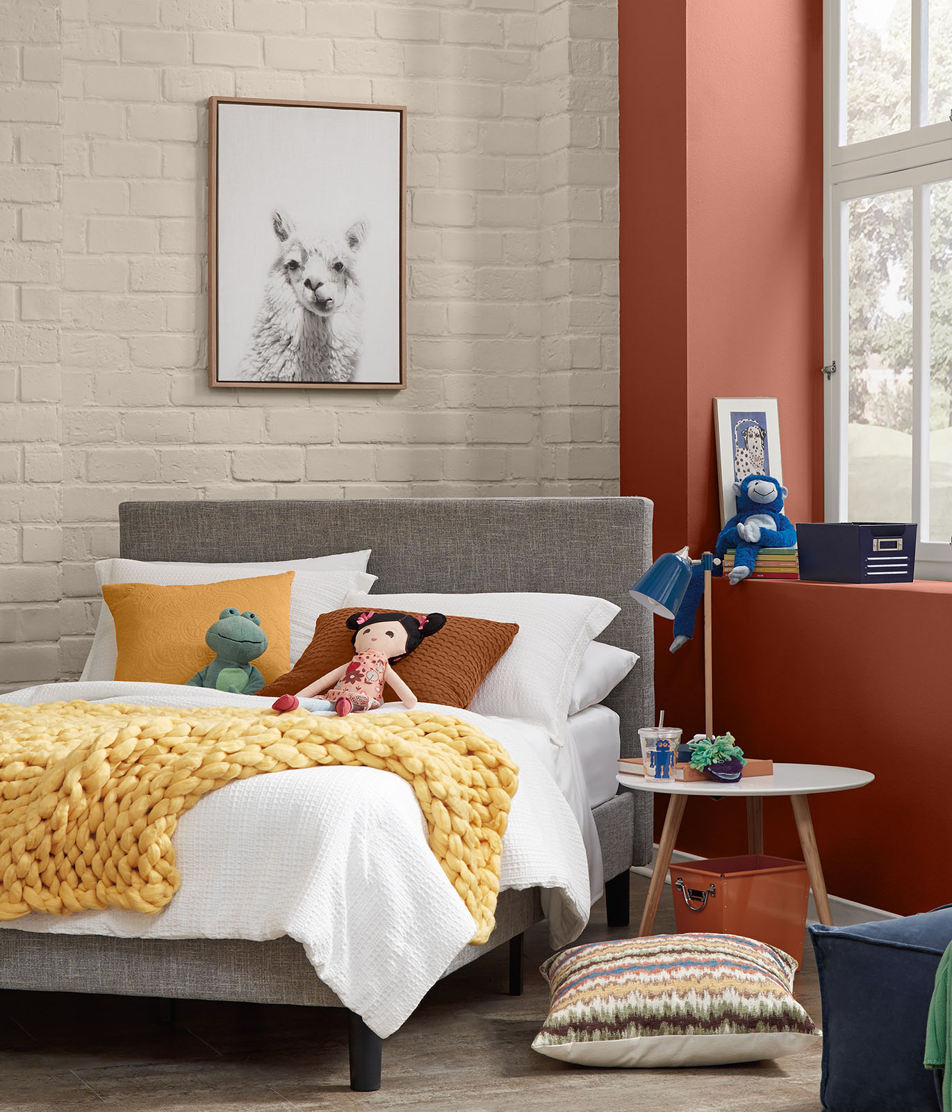 A child's bedroom with cream colored painted brick walls. The accent wall in painted in a dark orange color. The feeling of the room is cheerful.