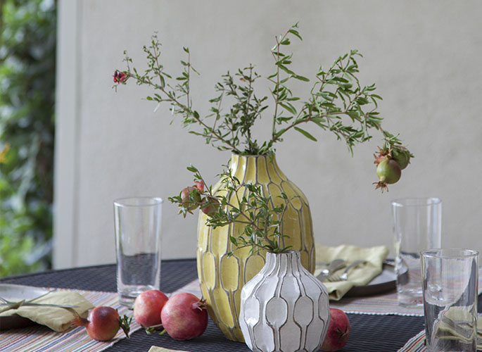 A tight crop showing a table sitting outside that is   dressed with white and yellow vases.  